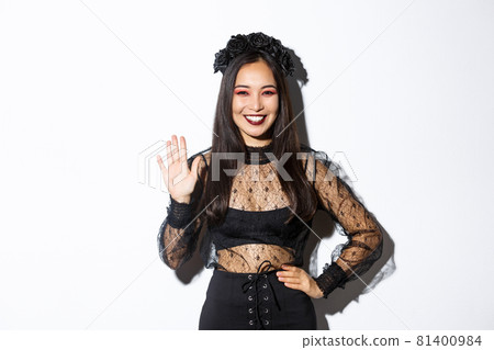 Image of friendly stylish asian woman in gothic lace dress waving hand to say hello, greeting someone, welcome people at halloween party, standing over white background Image of friendly stylish asian woman in gothic lace dress waving hand to say hello, greeting someone, welcome people at halloween party, standing over white background 81400984