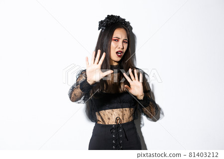 Image of bothered and annoyed asian woman in elegant gothic dress raising hands defensive, grimacing from camera flesh, asking to stop taking pictures of her, standing white background Image of bothered and annoyed asian woman in elegant gothic dress raising hands defensive, grimacing from camera flesh, asking to stop taking pictures of her, standing white background 81403212