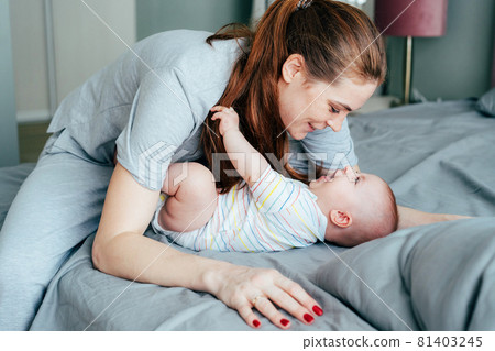 Happy mom cuddles her innocent adorable newborn baby in the morning in the bedroom. Happy mom cuddles her innocent adorable newborn baby in the morning in the bedroom. 81403245