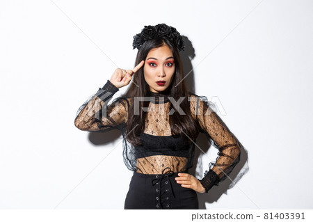 Image of annoyed young woman in halloween gothic dress scolding someone stupid, rolling finger on temple and looking at crazy person, standing over white background Image of annoyed young woman in halloween gothic dress scolding someone stupid, rolling finger on temple and looking at crazy person, standing over white background 81403391