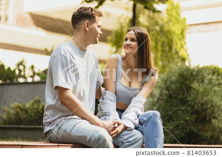 Cheerfull talk of young couple sitting on bench on summer day Cheerfull talk of young couple sitting on bench on summer day 81403653