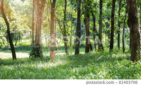 Young woman runner listening music on headphones while running on tropical rainforest trail in the morning. 81403706