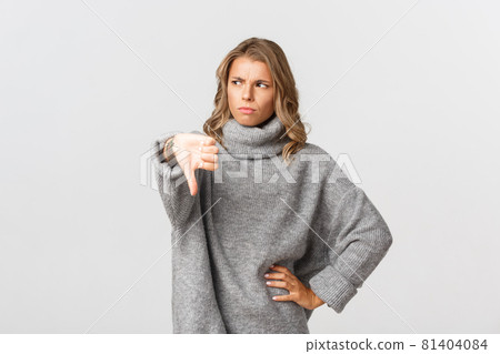 Young skeptical woman frowning and looking away, showing thumb-down, disappointed in something bad, standing over white background Young skeptical woman frowning and looking away, showing thumb-down, disappointed in something bad, standing over white background 81404084