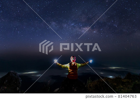 Hiker woman standing with hands up and Colorful night sky with stars. Background with galaxy. 81404763