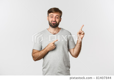 Skeptical and disappointed guy with beard, sulking and pointing at upper right corner, showing lame and unimpressive product, standing over white background Skeptical and disappointed guy with beard, sulking and pointing at upper right corner, showing lame and unimpressive product, standing over white background 81407844