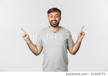 Portrait of happy smiling man with beard in gray t-shirt, pointing fingers sideways, showing two good choices, standing over white background 81408773