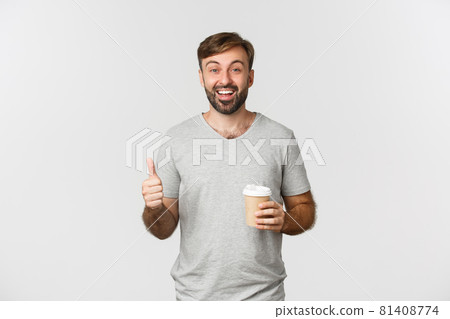 Portrait of cheerful caucasian man in gray t-shirt, drinking coffee and showing thumbs-up, recommend and like cafe, standing over white background 81408774
