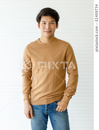 Medium shot portrait of a casual Asian handsome man with cute smiling in a soft brown long sleeve shirt and blue jeans with one hand in pocket posing isolated with white background in the studio Medium shot portrait of a casual Asian handsome man with cute smiling in a soft brown long sleeve shirt and blue jeans with one hand in pocket posing isolated with white background in the studio 81409734