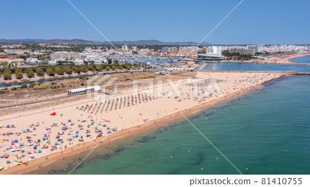 Aerial view of the luxury Falesia beach in Vilamoura. With sunbathing tourists on sun beds. Marina port with yachts, in the background. Aerial view of the luxury Falesia beach in Vilamoura. With sunbathing tourists on sun beds. Marina port with yachts, in the background. 81410755