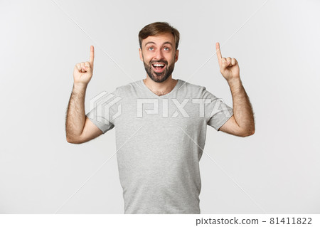 Portrait of happy surprised man with beard, looking fascinated and pointing fingers up, showing logo, standing over white background Portrait of happy surprised man with beard, looking fascinated and pointing fingers up, showing logo, standing over white background 81411822