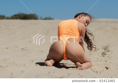 Seductive model in swimsuit kneeling on sandy beach Seductive model in swimsuit kneeling on sandy beach 81411865