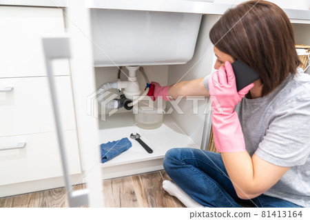 Woman sitting near leaking sink in laundry room calling for help Woman sitting near leaking sink in laundry room calling for help 81413164