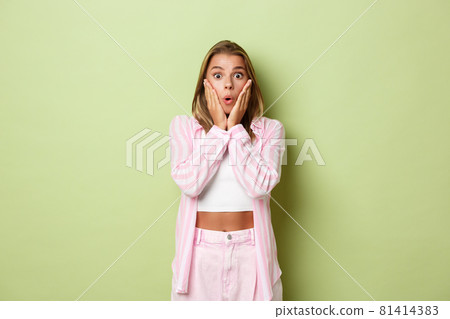 Portrait of attractive blond female model in pink outfit, looking surprised, gasping and staring at promo, standing over green background Portrait of attractive blond female model in pink outfit, looking surprised, gasping and staring at promo, standing over green background 81414383