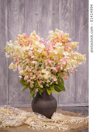 Bouquet of white with pink splashes of hydrangeas in a vase on the table against the background of a wooden wall. 81414994