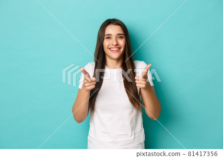 Cheerful brunette woman in white t-shirt, congratulating you, pointing fingers at camera, smiling pleased, recruiting people, standing over blue background Cheerful brunette woman in white t-shirt, congratulating you, pointing fingers at camera, smiling pleased, recruiting people, standing over blue background 81417356