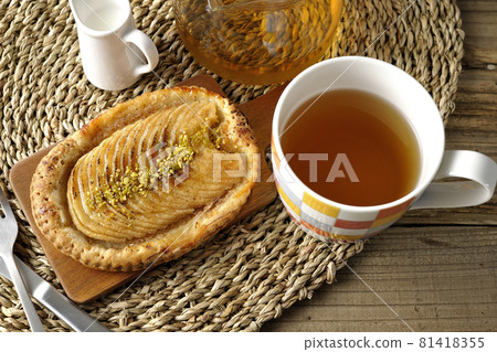 Pistachio and sliced apple tartlet on cutting board, tea, knife and fork Pistachio and sliced apple tartlet on cutting board, tea, knife and fork 81418355
