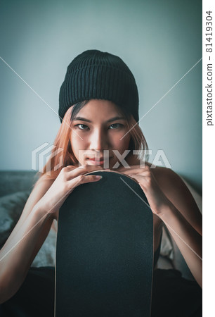 portrait of Asian girl with street fashion holding a skateboard on a sofa indoor. portrait of Asian girl with street fashion holding a skateboard on a sofa indoor. 81419304
