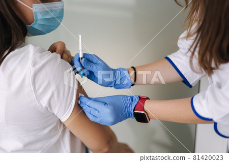 Woman in medical face mask getting Covid-19. Flu vaccine at the hospital. Professional nurse giving antiviral injection to female patient. Vaccination, disease prevention concept. Close-up of 81420023