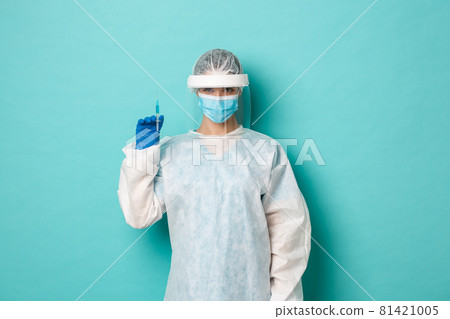 Concept of coronavirus, healthcare and quarantine. Image of female doctor in personal protective equipment, holding syringe with covid-19 vaccine, vaccinating patients 81421005