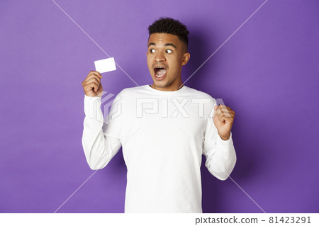 Impressed african-american guy, looking at credit card with amazement, standing over purple background Impressed african-american guy, looking at credit card with amazement, standing over purple background 81423291