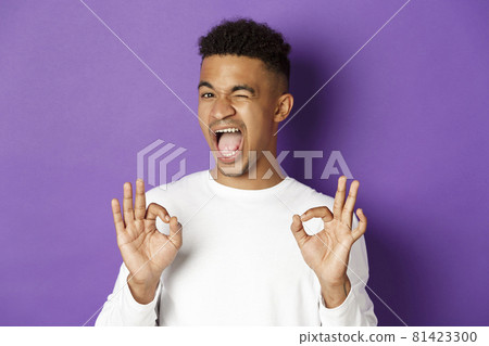 Cheeky african-american man winking, ensure you in something, showing okay signs in approval, standing pleased over purple background 81423300
