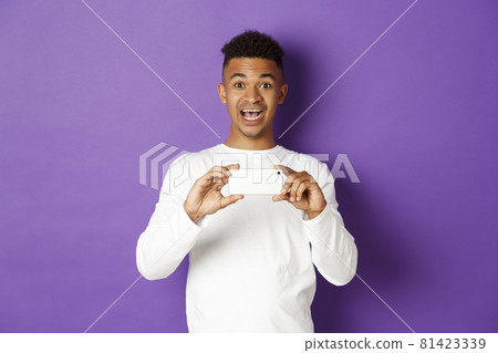 Young excited african-american guy taking pictures on smartphone, holding mobile phone and recording video with amazed face expression, standing over purple background Young excited african-american guy taking pictures on smartphone, holding mobile phone and recording video with amazed face expression, standing over purple background 81423339