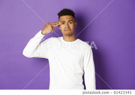 Image of sad and tired african-american male student, making finger gun sign over head and shooting himself, standing distressed against purple background Image of sad and tired african-american male student, making finger gun sign over head and shooting himself, standing distressed against purple background 81423341