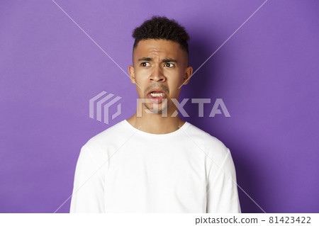 Image of shocked and startled african-american man, drop jaw and looking left at something embarrassing, standing over purple background Image of shocked and startled african-american man, drop jaw and looking left at something embarrassing, standing over purple background 81423422