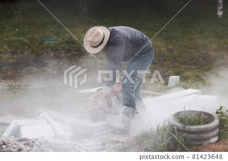 Worker mason cuts the sidewalk tile with circular saw while repairing sidewalk in city street 81423648