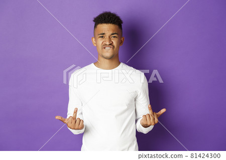 Image of arrogant and rude african-american guy in white sweatshirt, showing middle-finger, fuck you signs and grimacing, standing over purple background Image of arrogant and rude african-american guy in white sweatshirt, showing middle-finger, fuck you signs and grimacing, standing over purple background 81424300