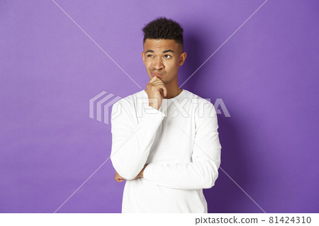 Portrait of young african-american male student thinking, looking at upper left corner thoughtful, making choice, standing over purple background with copy space Portrait of young african-american male student thinking, looking at upper left corner thoughtful, making choice, standing over purple background with copy space 81424310