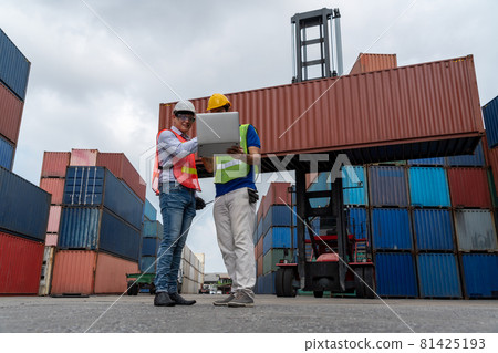 Industrial worker works with co-worker at overseas shipping container yard Industrial worker works with co-worker at overseas shipping container yard 81425193