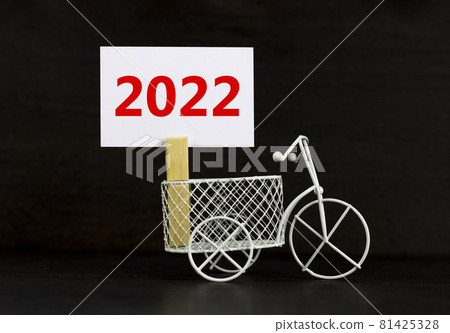 2022 happy new year symbol. Wooden clothespin, white sheet of paper with number 2022. Miniature bicycle model. Beautiful black background, copy space. Business and 2022 happy new year concept. 2022 happy new year symbol. Wooden clothespin, white sheet of paper with number 2022. Miniature bicycle model. Beautiful black background, copy space. Business and 2022 happy new year concept. 81425328