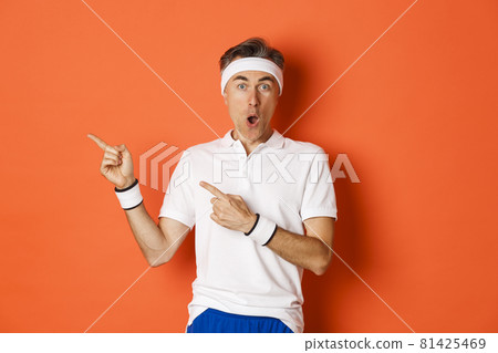 Portrait of surprised middle-aged man doing sports, showing something amazing, pointing fingers left and looking fascinated, wearing activewear for workout, standing over white background Portrait of surprised middle-aged man doing sports, showing something amazing, pointing fingers left and looking fascinated, wearing activewear for workout, standing over white background 81425469