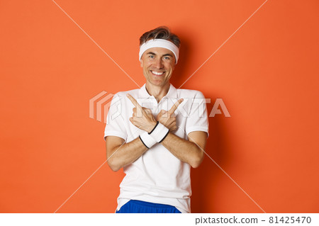 Concept of sport, fitness and lifestyle. Portrait of happy, handsome middle-aged guy in workout clothes, pointing fingers sideways, showing left and right promo banners, orange background Concept of sport, fitness and lifestyle. Portrait of happy, handsome middle-aged guy in workout clothes, pointing fingers sideways, showing left and right promo banners, orange background 81425470