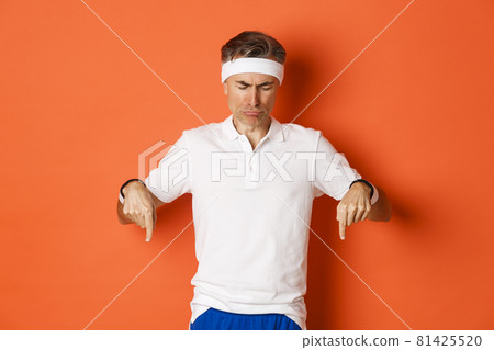 Concept of workout, sports and lifestyle. Image of disappointed and sad adult sportsman, looking and pointing down distressed, frowning upset, standing over orange background 81425520