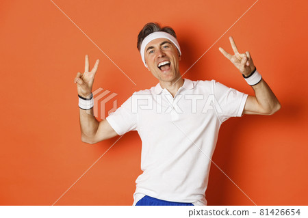 Image of happy and healthy middle-aged man in sport clothing, showing peace signs and smiling, workout over orange background Image of happy and healthy middle-aged man in sport clothing, showing peace signs and smiling, workout over orange background 81426654