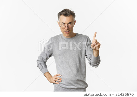 Image of handsome middle-aged man in glasses and grey sweater, showing one finger, teaching a lesson, standing over white background Image of handsome middle-aged man in glasses and grey sweater, showing one finger, teaching a lesson, standing over white background 81426670