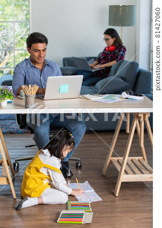 Mixed race family sharing time in living room. Caucasian father using notebook computer to work and half-Thai playing and painting under desk while Asian mother with laptop working her job on sofa Mixed race family sharing time in living room. Caucasian father using notebook computer to work and half-Thai playing and painting under desk while Asian mother with laptop working her job on sofa 81427060