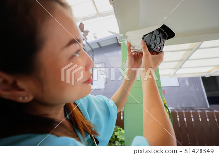 Beautiful woman house adjusts direction angle view of CCTV home security camera and fine-tune internet cam for perfect scene of watching. Conept for self-reliant and DIY job of modern housewife. Beautiful woman house adjusts direction angle view of CCTV home security camera and fine-tune internet cam for perfect scene of watching. Conept for self-reliant and DIY job of modern housewife. 81428349