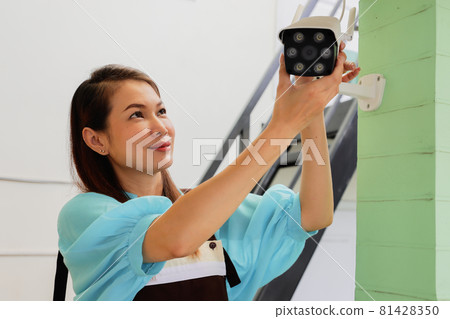 Beautiful woman house adjusts direction angle view of CCTV home security camera and fine-tune internet cam for perfect scene of watching. Conept for self-reliant and DIY job of modern housewife. 81428350