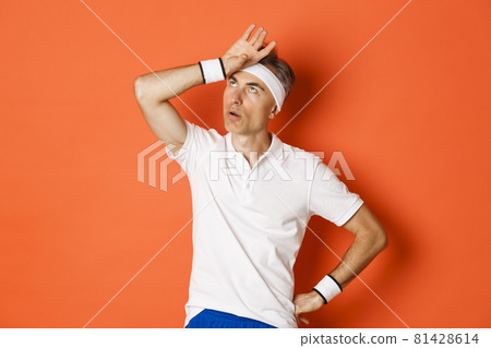 Concept of sport, fitness and lifestyle. Portrait of annoyed male athlete, roll eyes and facepalm, looking bothered, standing over orange background Concept of sport, fitness and lifestyle. Portrait of annoyed male athlete, roll eyes and facepalm, looking bothered, standing over orange background 81428614