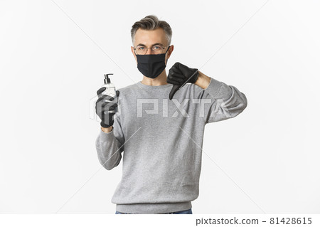 Concept of coronavirus, lifestyle and quarantine. Portrait of middle-aged man in medical mask and gloves do not recommend antiseptic, showing hand sanitizer and thumbs-down, white background Concept of coronavirus, lifestyle and quarantine. Portrait of middle-aged man in medical mask and gloves do not recommend antiseptic, showing hand sanitizer and thumbs-down, white background 81428615