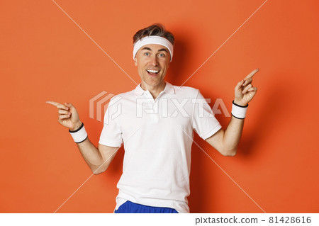 Concept of sport, fitness and lifestyle. Cheerful middle-aged sportsman with headband, smiling happy and pointing fingers sideways, showing left and right copy space Concept of sport, fitness and lifestyle. Cheerful middle-aged sportsman with headband, smiling happy and pointing fingers sideways, showing left and right copy space 81428616
