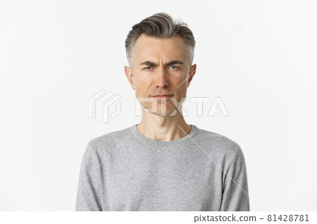 Close-up of skeptical middle-aged man, frowning and looking doubtful at camera, standing over white background in gray sweater Close-up of skeptical middle-aged man, frowning and looking doubtful at camera, standing over white background in gray sweater 81428781