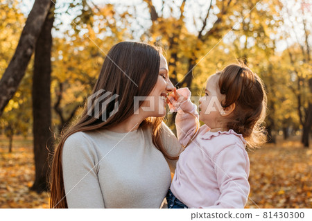 Happy family mom and toddler baby girl playing outdoors in fall park. Little girl and her mother in the autumn park. Fall activities for toddlers Happy family mom and toddler baby girl playing outdoors in fall park. Little girl and her mother in the autumn park. Fall activities for toddlers 81430300