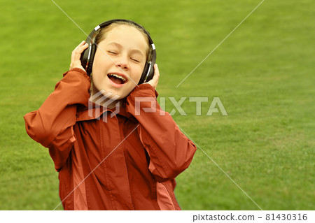 Teenage girl listening to music. Female young girl outside in autumn park listening to music on headphones. 81430316