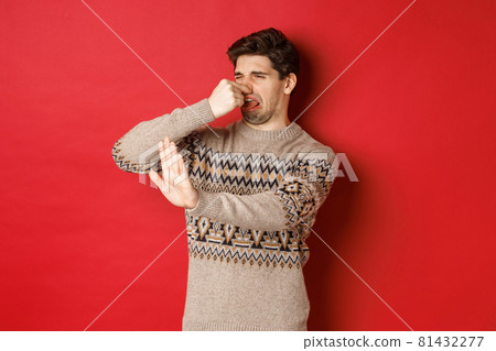 Image of disgusted handsome man in winter sweater, rejecting something with bad smell, shut nose and raising hand to decline, standing over red background Image of disgusted handsome man in winter sweater, rejecting something with bad smell, shut nose and raising hand to decline, standing over red background 81432277