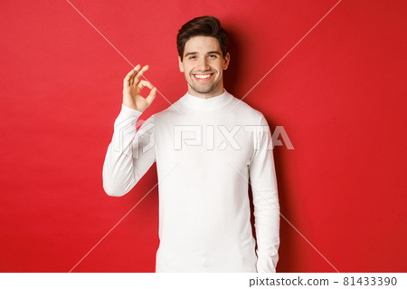 Portrait of happy and satisfied handsome man, wearing white sweater, showing okay sign and smiling, approve something good, recommending shop, standing over red background Portrait of happy and satisfied handsome man, wearing white sweater, showing okay sign and smiling, approve something good, recommending shop, standing over red background 81433390