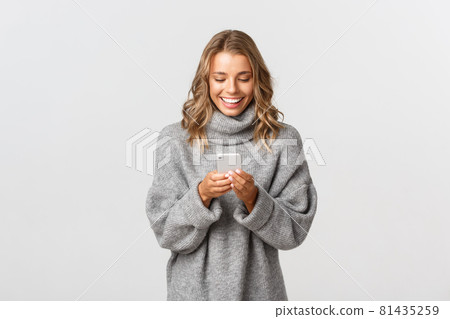 Portrait of young happy woman with short blond hair, using mobile phone and smiling, shopping online or sending message, standing over white background Portrait of young happy woman with short blond hair, using mobile phone and smiling, shopping online or sending message, standing over white background 81435259